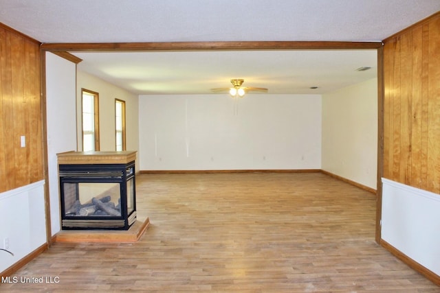unfurnished living room featuring baseboards, a ceiling fan, wood finished floors, and wood walls