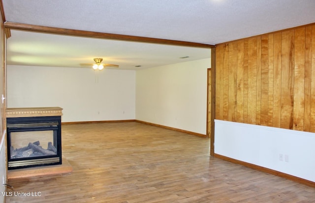 unfurnished living room with a multi sided fireplace, ceiling fan, wood finished floors, baseboards, and wooden walls