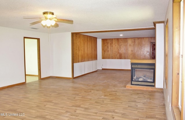 unfurnished living room with a multi sided fireplace, a ceiling fan, a textured ceiling, wood finished floors, and baseboards