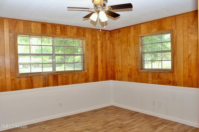 unfurnished room with wooden walls, a textured ceiling, ceiling fan, and a healthy amount of sunlight