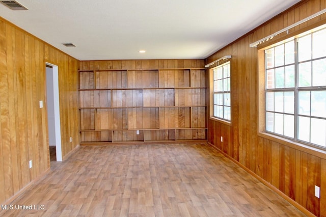 empty room with wooden walls, baseboards, visible vents, and wood finished floors