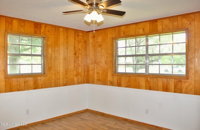 unfurnished room featuring a ceiling fan, wood walls, plenty of natural light, and wood finished floors