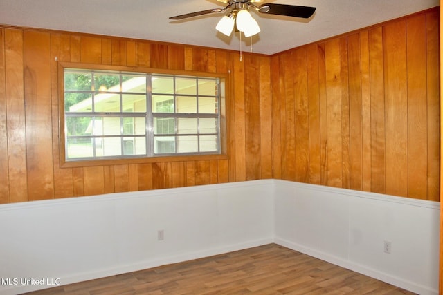 empty room with ceiling fan, wood finished floors, and wooden walls