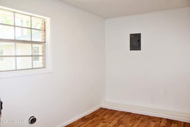 empty room featuring baseboards, crown molding, wood finished floors, and electric panel