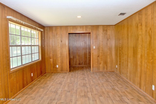 empty room featuring visible vents, wood walls, baseboards, and wood finished floors