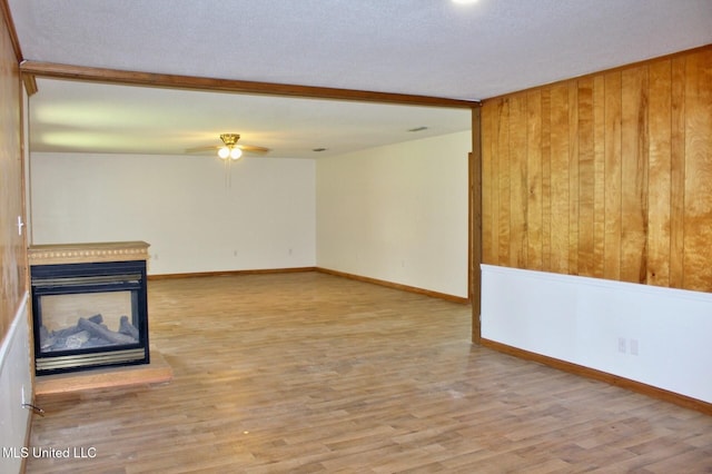 unfurnished living room featuring wooden walls, a multi sided fireplace, ceiling fan, and wood finished floors