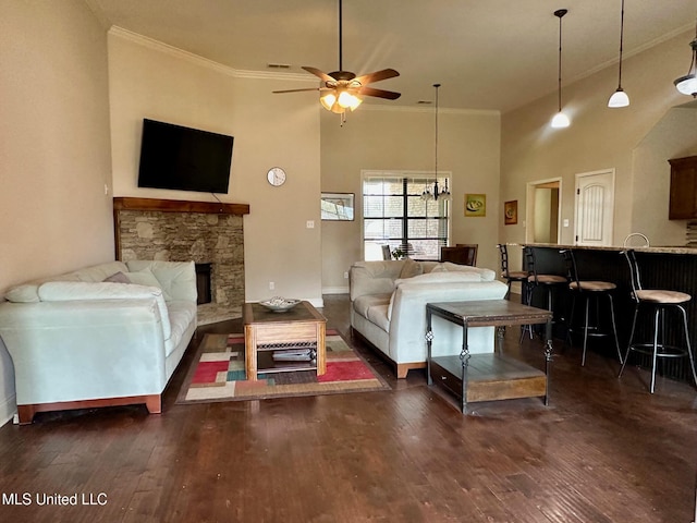 living room featuring dark wood-type flooring, a stone fireplace, crown molding, a towering ceiling, and ceiling fan