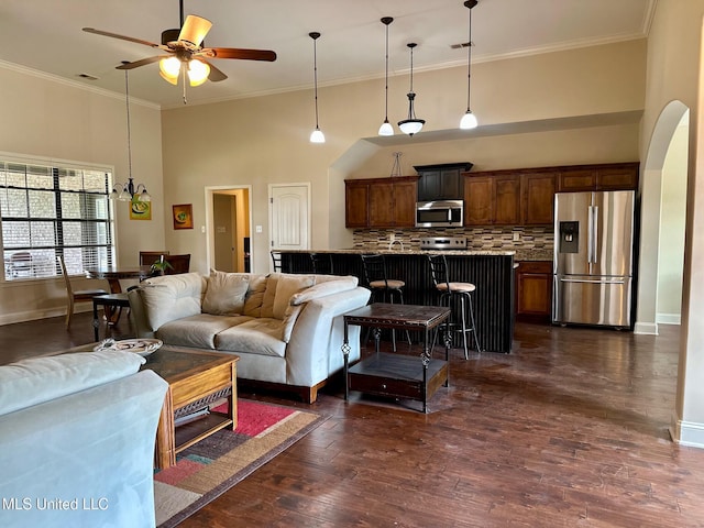 living room with dark hardwood / wood-style flooring, a towering ceiling, ceiling fan with notable chandelier, and ornamental molding