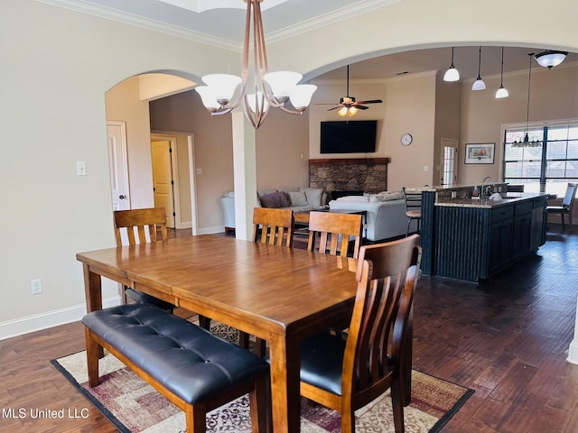 dining room with sink, a fireplace, ornamental molding, dark hardwood / wood-style flooring, and ceiling fan with notable chandelier