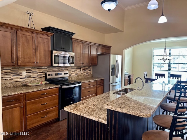 kitchen featuring decorative light fixtures, stainless steel appliances, an island with sink, and a breakfast bar