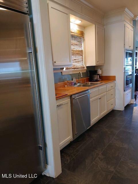 kitchen featuring ornamental molding, white cabinetry, stainless steel appliances, and a sink