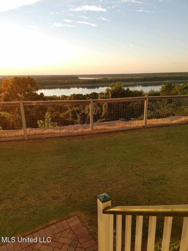 yard at dusk featuring a water view and fence