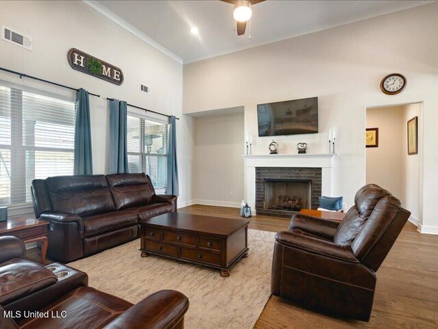 living room featuring a brick fireplace, ornamental molding, ceiling fan, wood-type flooring, and a high ceiling