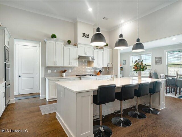 kitchen with a center island with sink, pendant lighting, and white cabinets