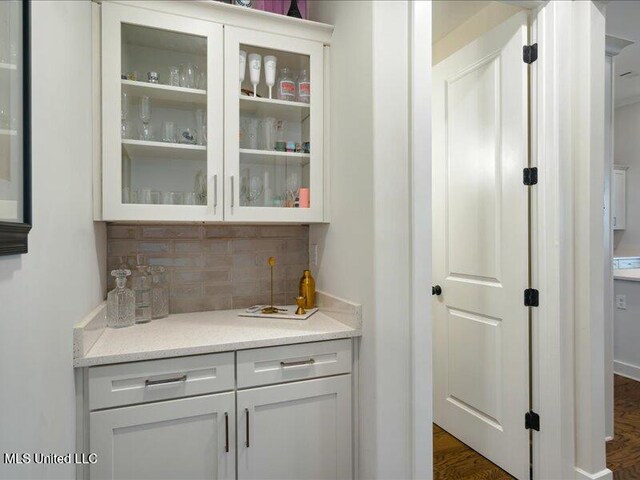 bar with backsplash, light stone countertops, white cabinets, and dark wood-type flooring