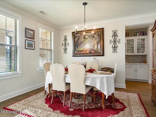 dining room with dark wood-type flooring, plenty of natural light, crown molding, and a notable chandelier