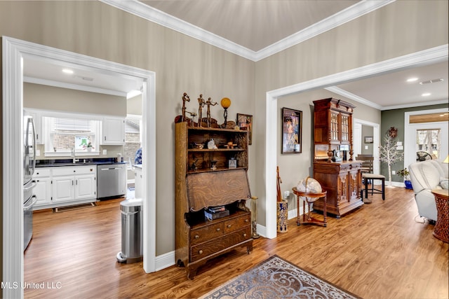 hallway featuring visible vents, baseboards, light wood-type flooring, ornamental molding, and a sink