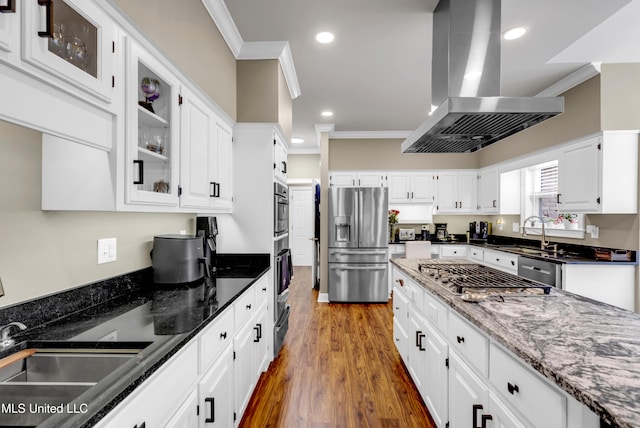 kitchen featuring ornamental molding, dark stone countertops, appliances with stainless steel finishes, island range hood, and a sink