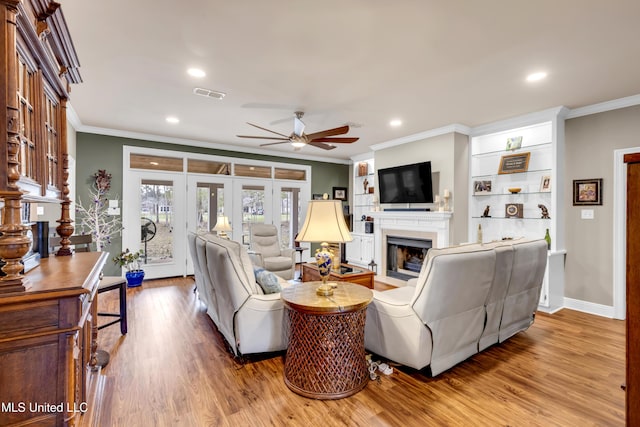 living room with wood finished floors, visible vents, a fireplace with flush hearth, and ornamental molding