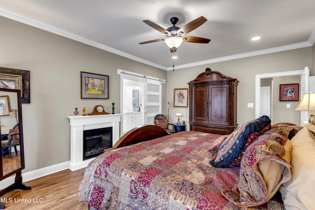 bedroom featuring ornamental molding, a glass covered fireplace, wood finished floors, a barn door, and baseboards