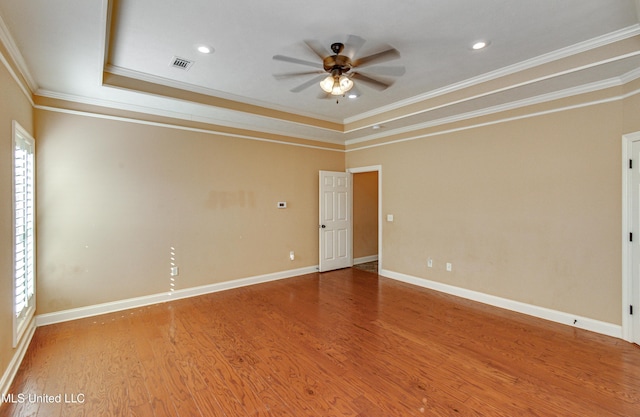 spare room with plenty of natural light, a raised ceiling, wood-type flooring, and crown molding