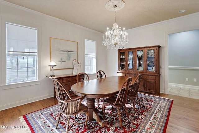 dining space featuring light wood-style flooring, a notable chandelier, baseboards, and ornamental molding