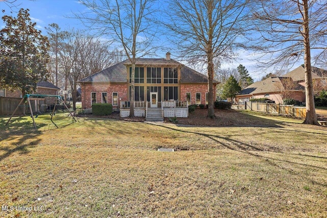 rear view of house with fence, a yard, a sunroom, brick siding, and a chimney