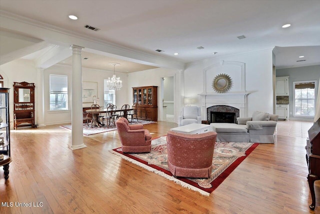 living area featuring light wood finished floors, visible vents, ornamental molding, a fireplace, and ornate columns