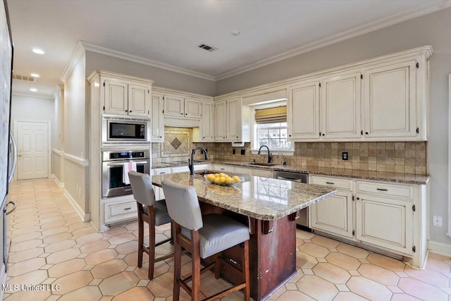 kitchen with light stone countertops, an island with sink, a sink, decorative backsplash, and appliances with stainless steel finishes