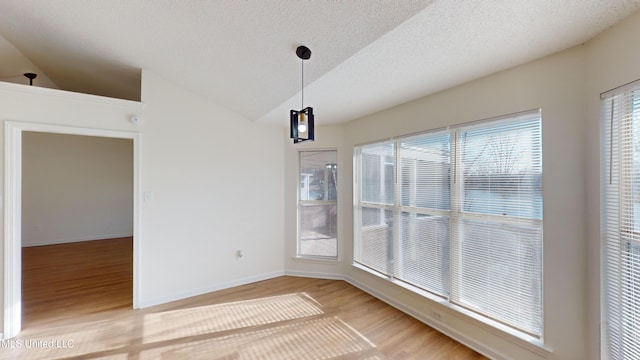 unfurnished dining area featuring hardwood / wood-style flooring, vaulted ceiling, and a textured ceiling