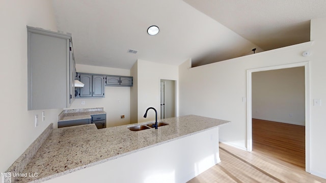 kitchen featuring sink, gray cabinetry, light stone counters, kitchen peninsula, and light wood-type flooring