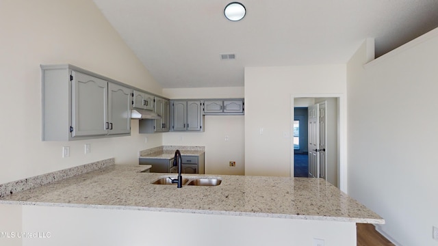 kitchen with lofted ceiling, sink, gray cabinetry, light stone countertops, and kitchen peninsula