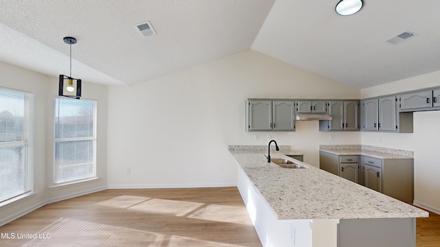 kitchen featuring gray cabinets, vaulted ceiling, decorative light fixtures, sink, and hardwood / wood-style flooring