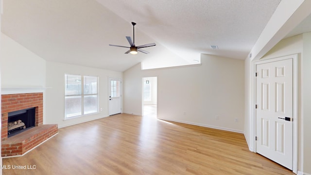 unfurnished living room with lofted ceiling, ceiling fan, light hardwood / wood-style floors, a textured ceiling, and a brick fireplace