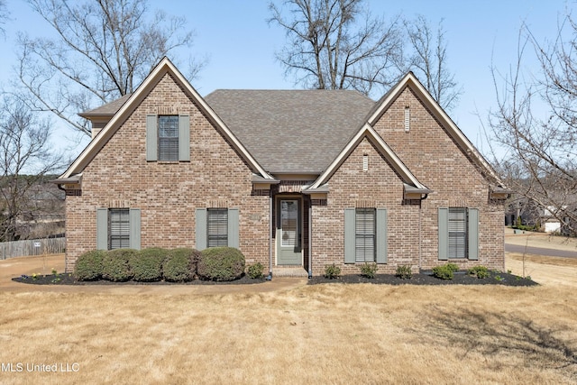 view of front of property featuring brick siding, roof with shingles, and a front yard