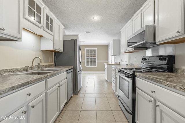 kitchen featuring a sink, stainless steel appliances, white cabinets, light tile patterned floors, and glass insert cabinets