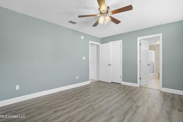 unfurnished bedroom featuring visible vents, a textured ceiling, wood finished floors, connected bathroom, and baseboards