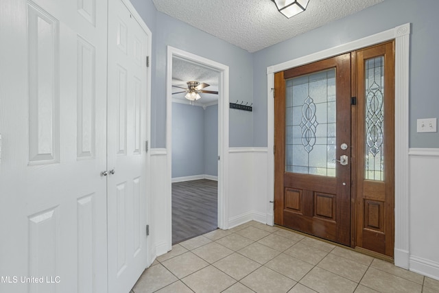 foyer entrance featuring light tile patterned floors, a textured ceiling, ceiling fan, and wainscoting
