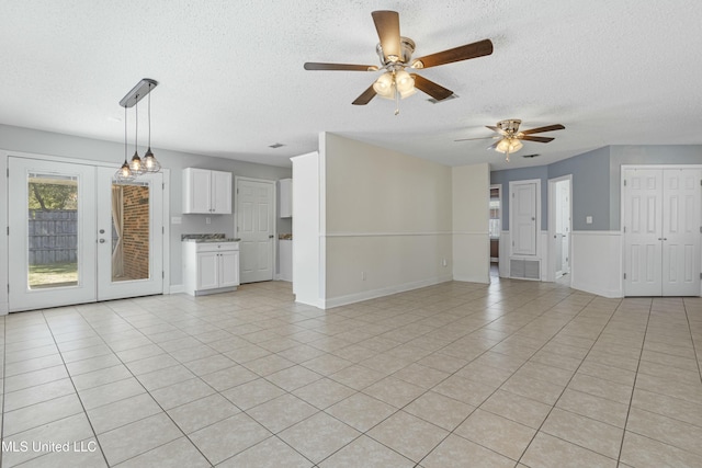 unfurnished living room with light tile patterned floors, baseboards, a textured ceiling, and ceiling fan