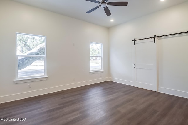 empty room with ceiling fan, a barn door, and dark hardwood / wood-style flooring