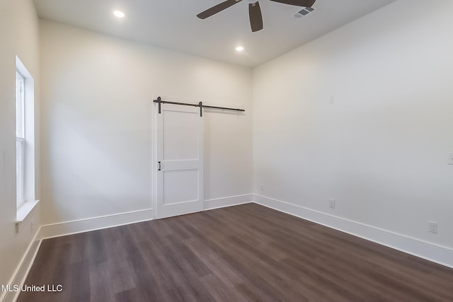 unfurnished room featuring dark wood-type flooring, ceiling fan, and a barn door