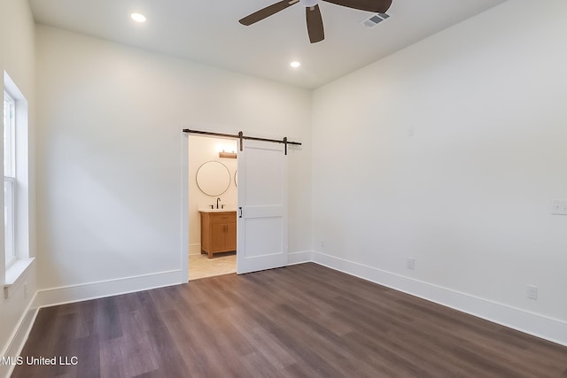 spare room featuring sink, wood-type flooring, a barn door, and ceiling fan