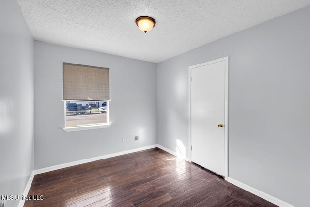 spare room featuring dark wood finished floors, a textured ceiling, and baseboards