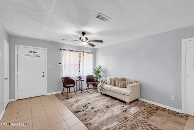 living area featuring light tile patterned floors, visible vents, baseboards, ceiling fan, and a textured ceiling