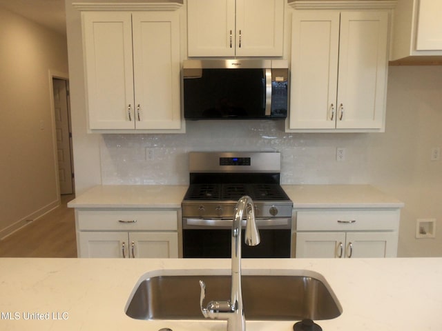 kitchen featuring sink, hardwood / wood-style flooring, appliances with stainless steel finishes, white cabinetry, and backsplash