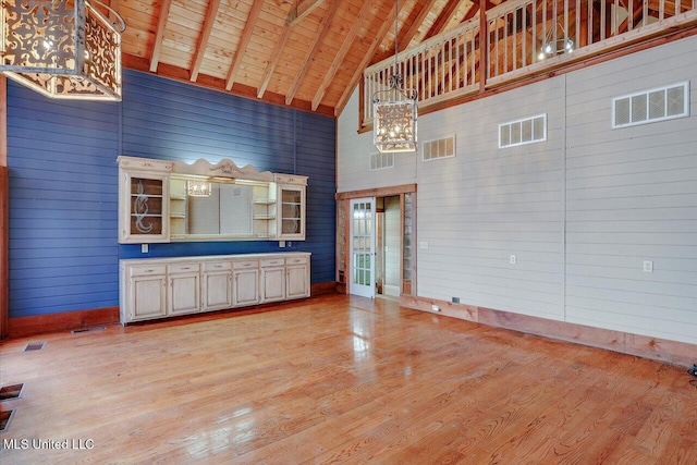 unfurnished living room with wooden ceiling, high vaulted ceiling, wooden walls, light wood-type flooring, and beam ceiling