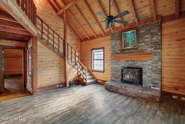 unfurnished living room with a wood stove, wooden walls, beamed ceiling, and wood ceiling