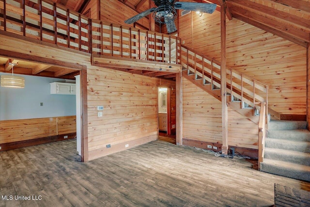 unfurnished living room featuring wood walls, wooden ceiling, ceiling fan, beam ceiling, and wood-type flooring