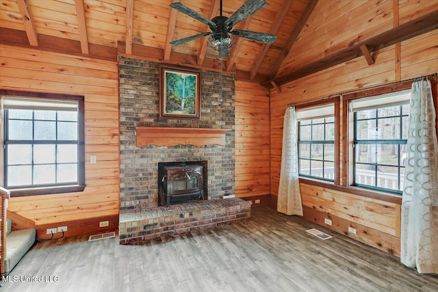 unfurnished living room with a wood stove, ceiling fan, vaulted ceiling with beams, wood-type flooring, and wooden walls