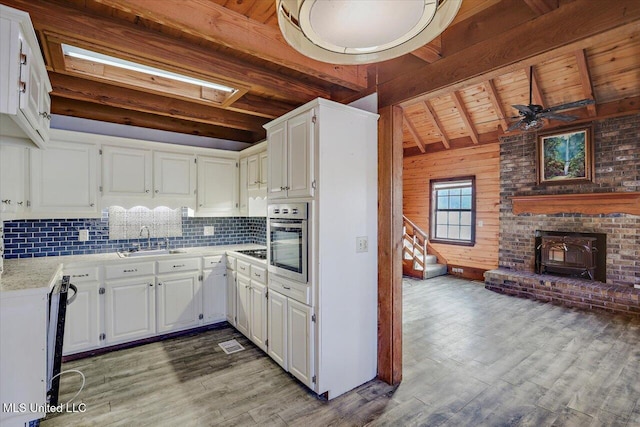 kitchen featuring a wood stove, white cabinetry, stainless steel oven, ceiling fan, and sink